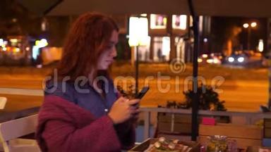 年轻的红海妇女在街边的咖啡馆里，在她的食物上拍照，灯。 3840x2160